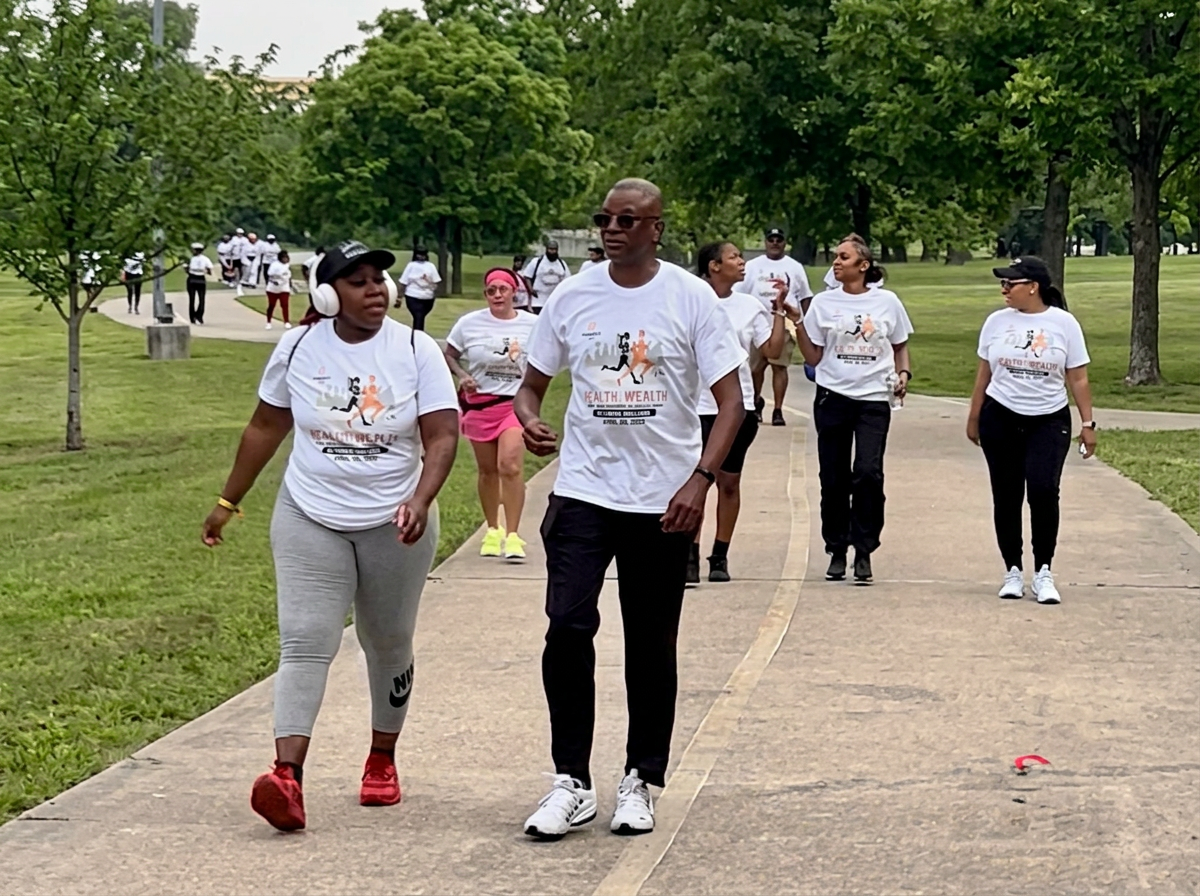 Corey Artis walking with community members at the Health & Wealth Walk wearing event t-shirts