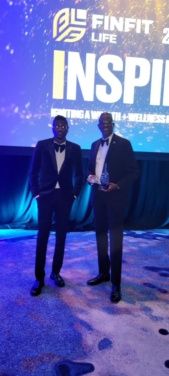 Corey Artis with his son at the FinFit Life Inspire awards holding a recognition trophy